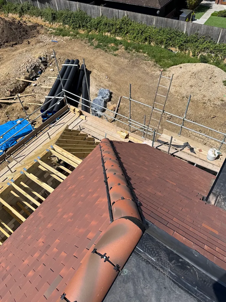 New tiled roof with bedded ridge tiles beside open rafters and scaffold